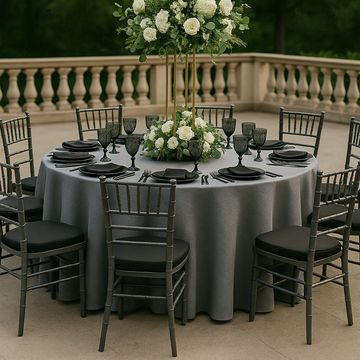 Mesa redonda con mantel gris obscuro y arreglo floral de Alfa y Omega con bajaplato, sillas chiavari