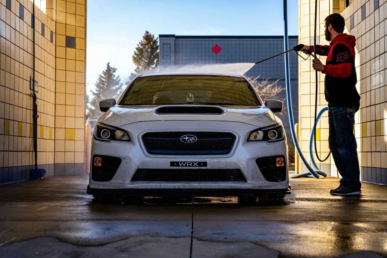 A man spraying his car with water washing the soap off