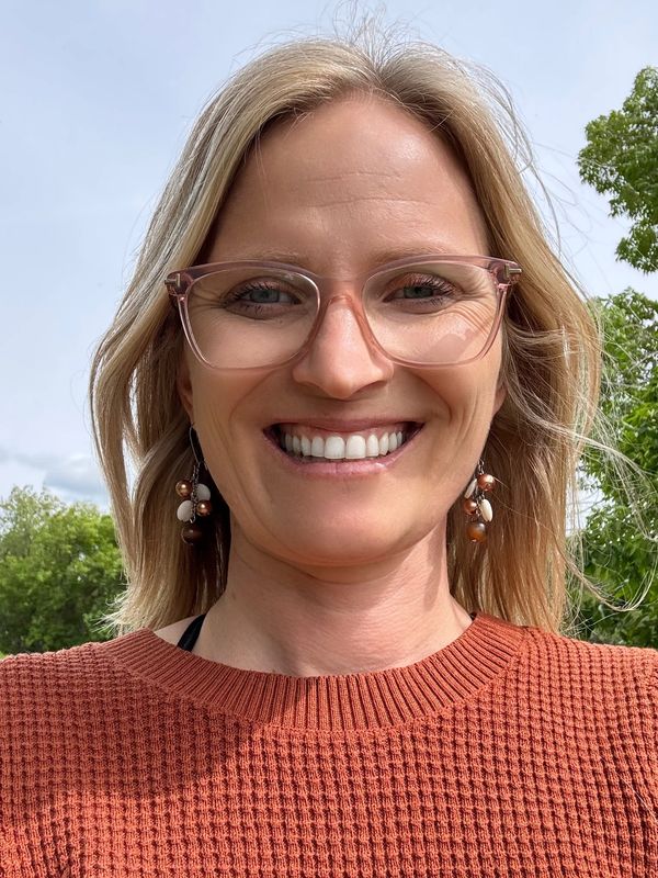 Smiling woman wearing glasses and earrings outdoors.