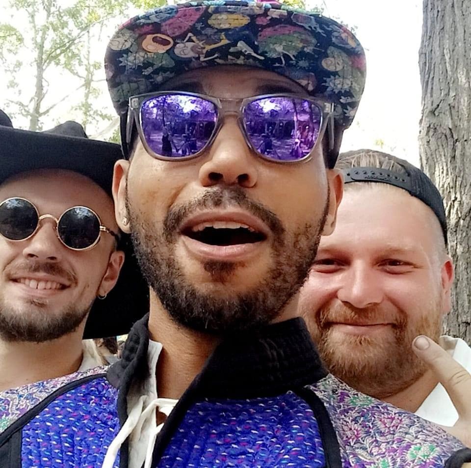 Three men posing for a cheerful selfie outdoors, wearing hats and sunglasses.