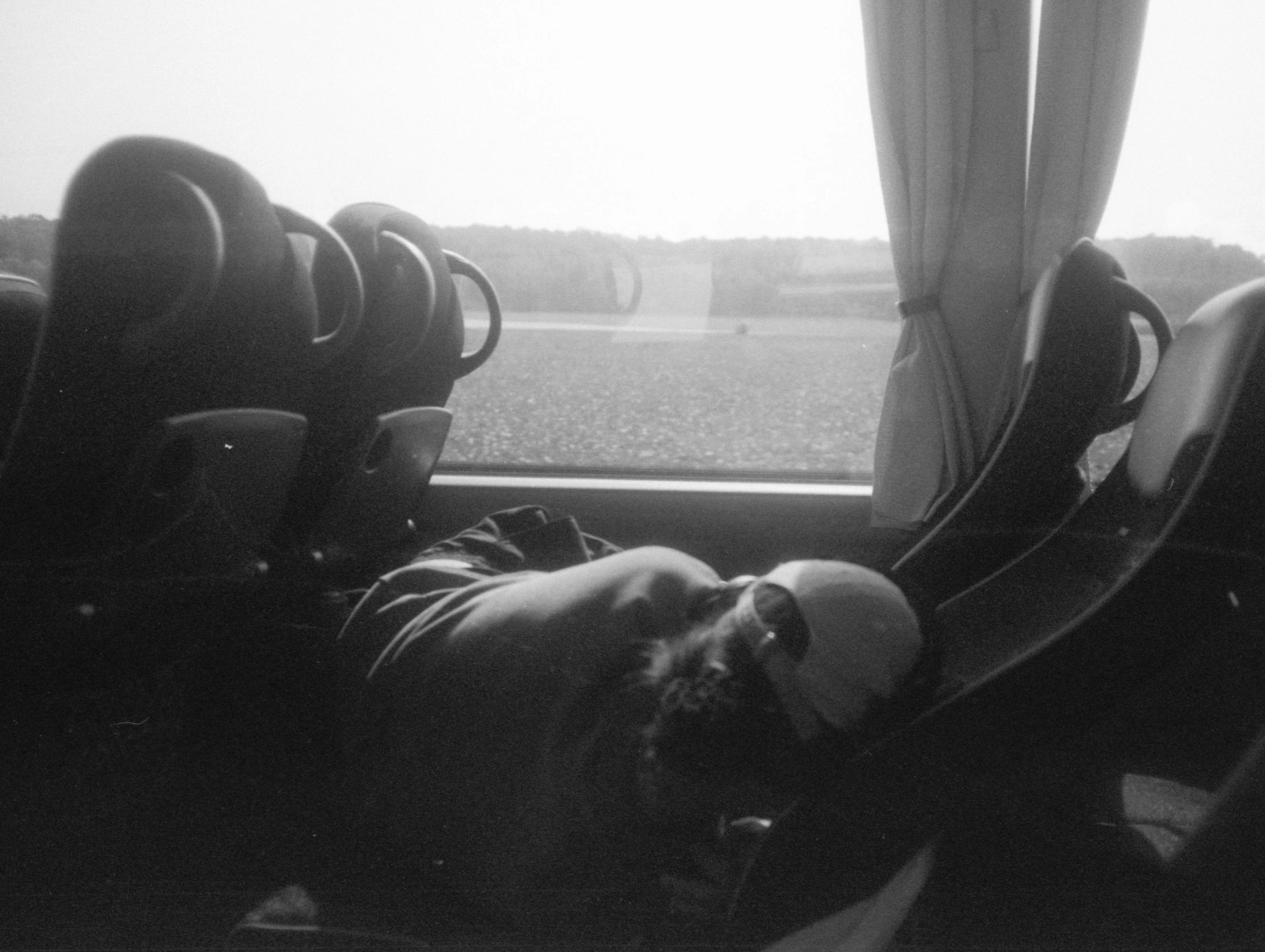 Person resting on a bus seat with a countryside view outside.