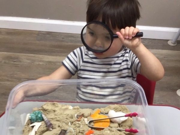 Child exploring sand table with magnifying glass.