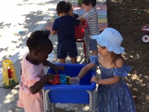Two kids playing with water outside in a blue tub.
