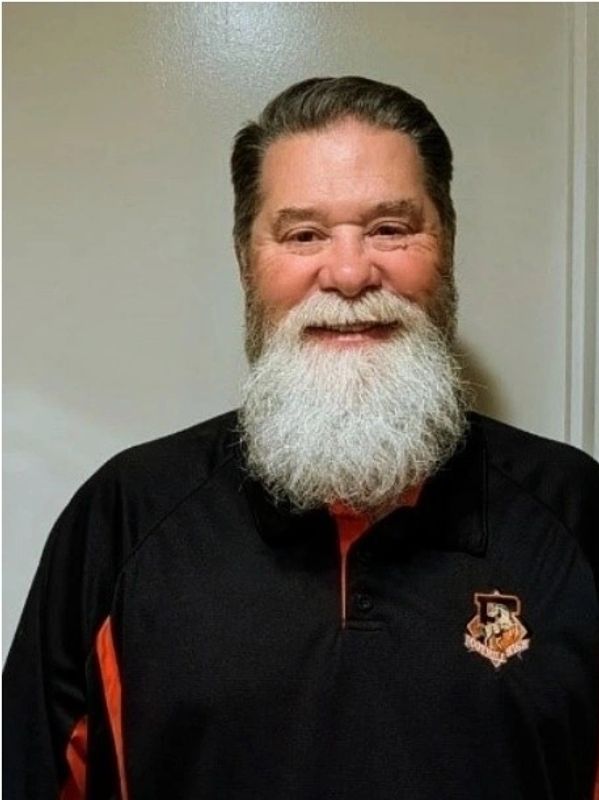 Smiling man with a long white beard in black and orange shirt.