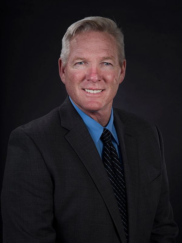 Smiling middle-aged man in a suit against a dark backdrop.