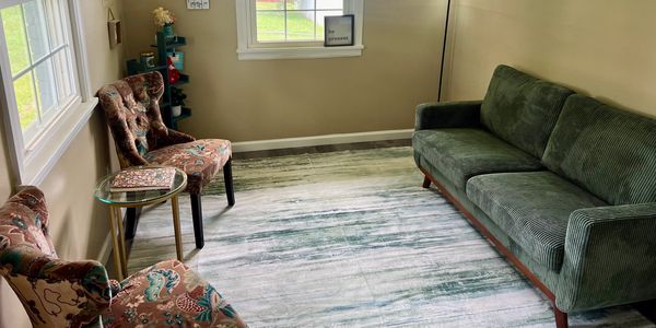 Cozy living room with green sofa and floral chairs around a light rug.