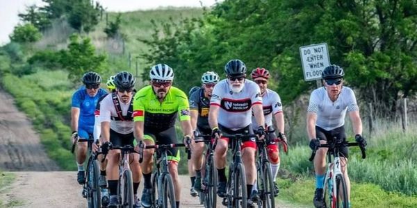 Group of cyclists riding on a rural dirt road surrounded by greenery.