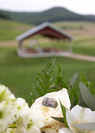 Wedding rings nestled in white flowers with a blurred outdoor pavilion in the background.