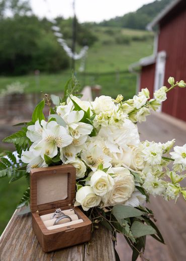 A wooden box with rings beside a white flower bouquet on a rustic wooden railing.