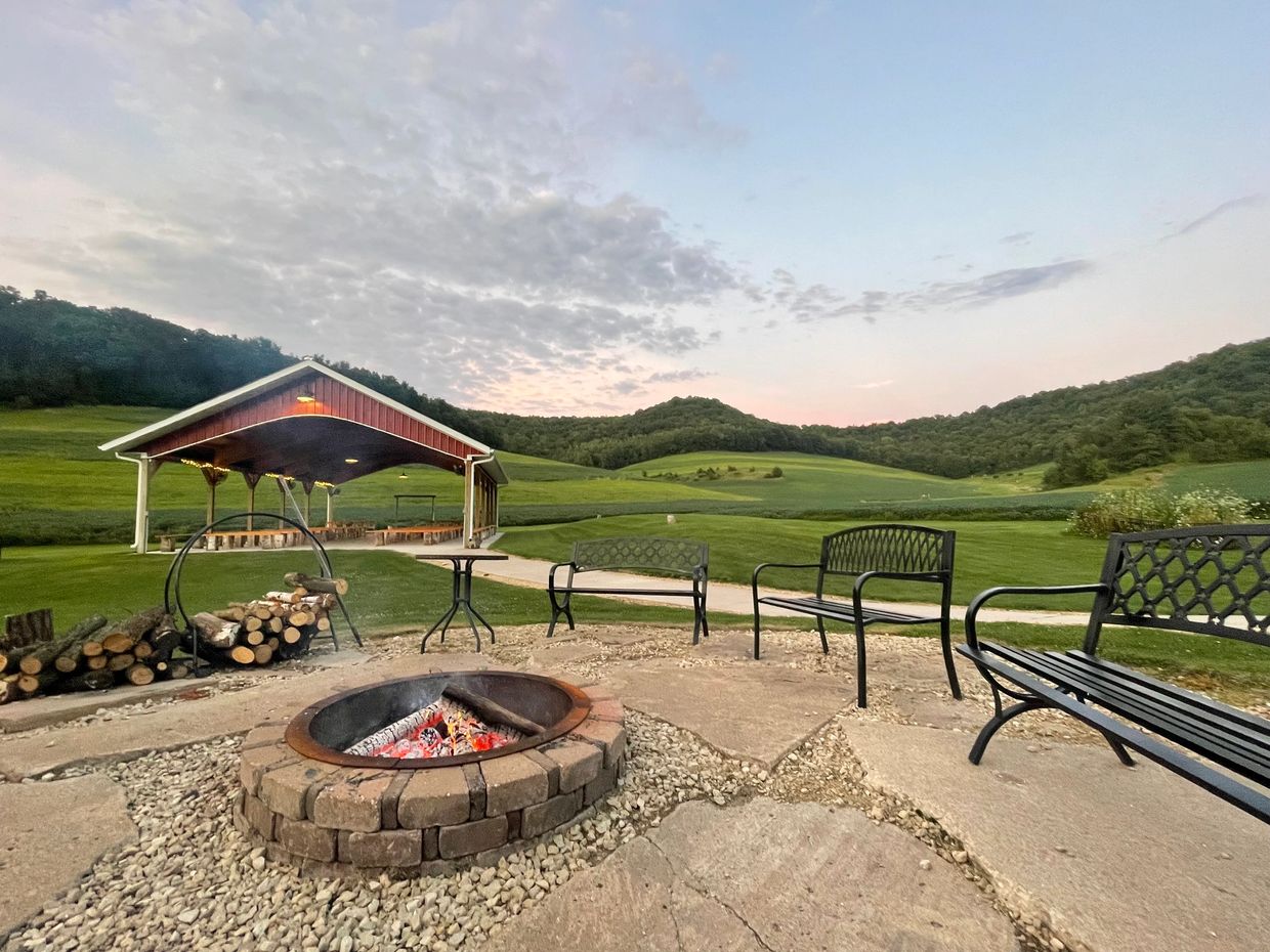 Outdoor fire pit with benches and pavilion in a serene green landscape.