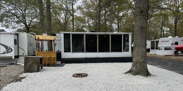 A cozy screened porch attached to a trailer in a wooded RV park.