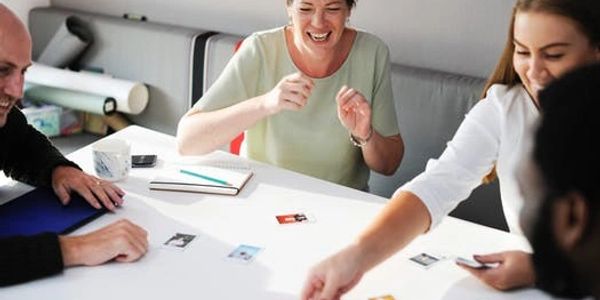 Four people joyfully playing a board game around a white table.