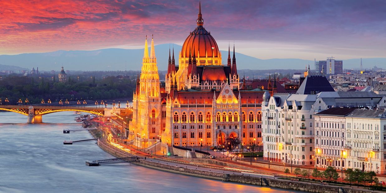 Illuminated historic building by the river at sunset with a vibrant sky.