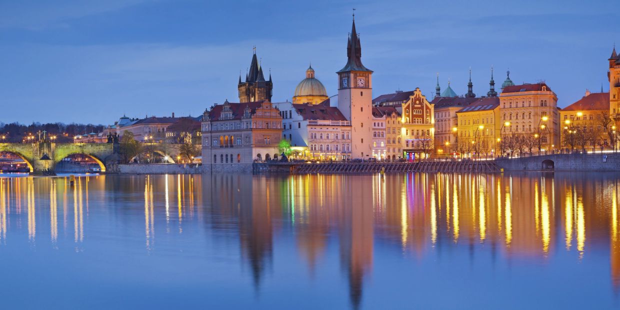 Evening cityscape with historic buildings reflecting on calm river water.