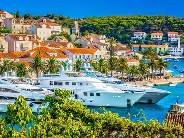 Yachts docked at a vibrant coastal town with red-roofed buildings and palm trees.