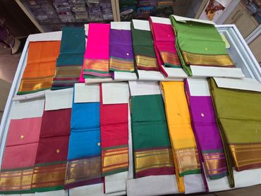 Colorful traditional silk sarees with golden borders displayed on a white surface.
