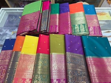 Colorful silk sarees with intricate gold borders displayed on a glass surface.