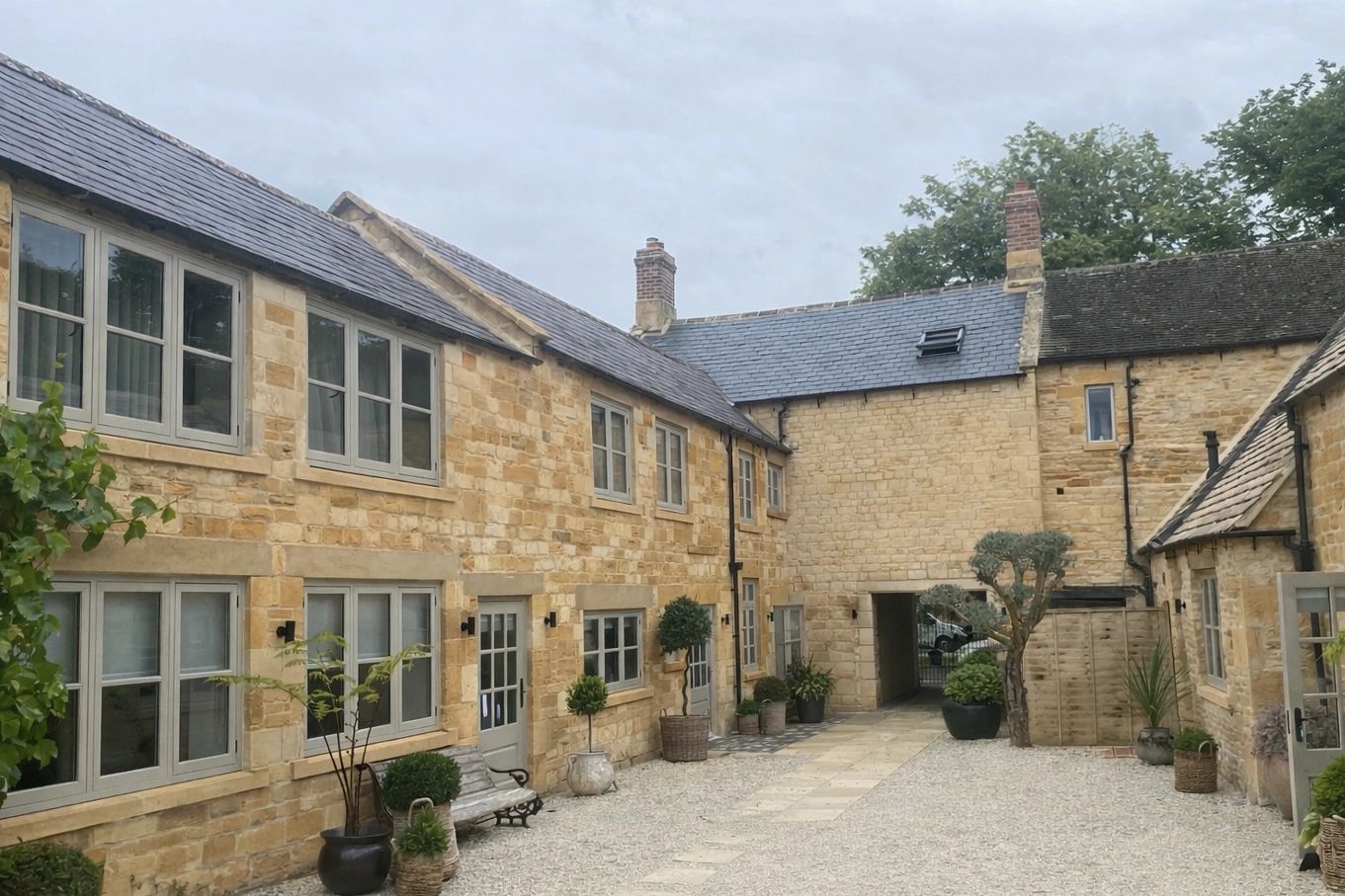 Stone buildings with a courtyard and potted plants under a cloudy sky.