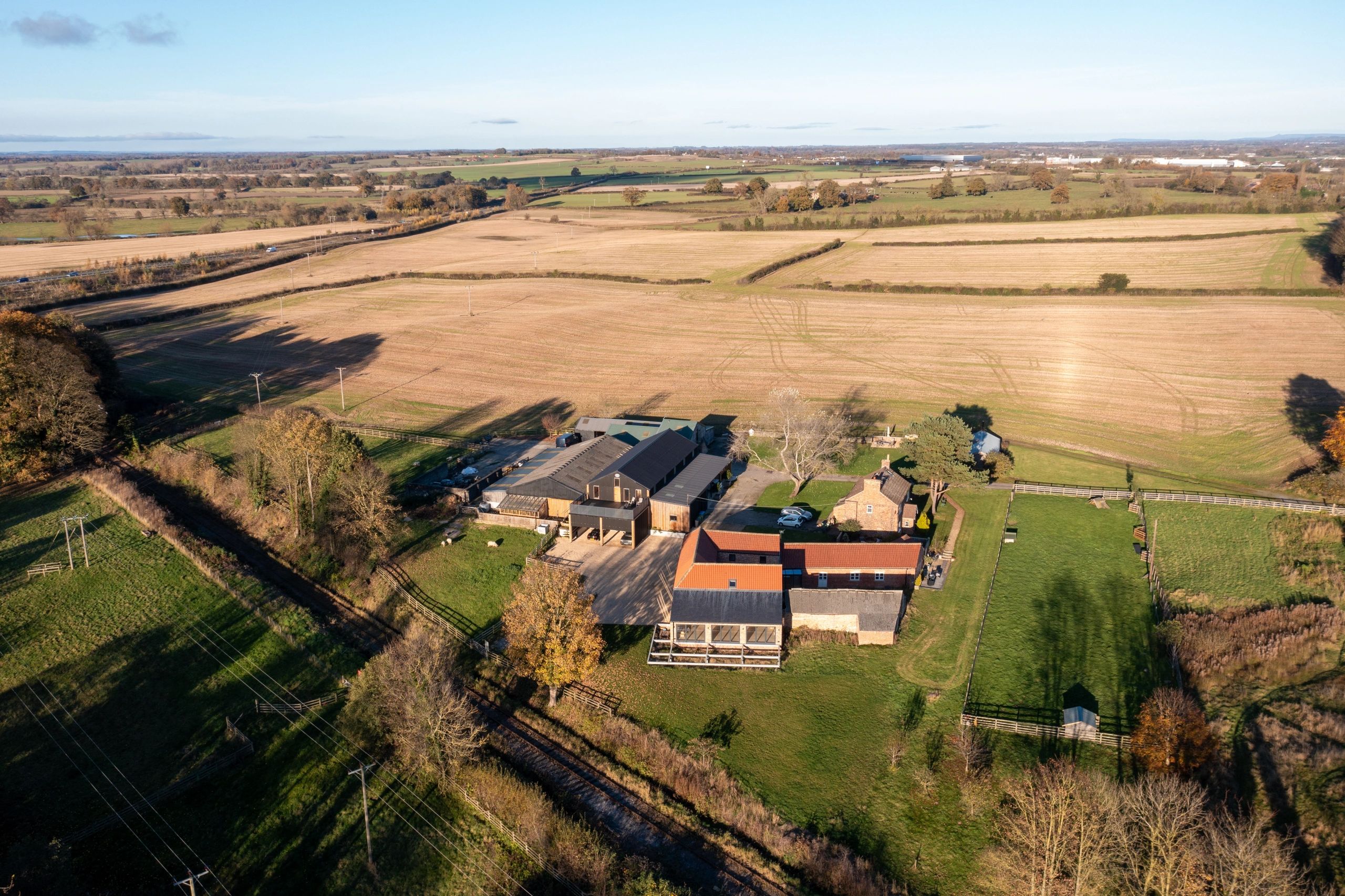 Aerial view of a rural farm with fields and buildings under clear blue sky.