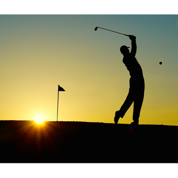 Silhouette of a golfer swinging at sunset near the flag on the green.