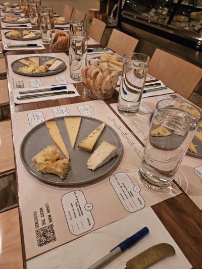 A long table set for a cheese tasting event with plates, glasses, bread, and tasting notes.