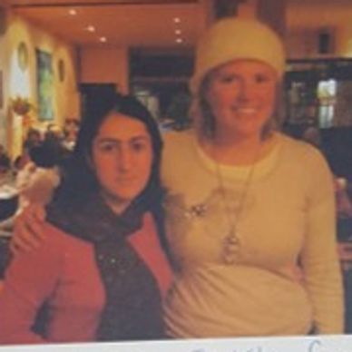 Two women posing together indoors, one wearing a light hat.