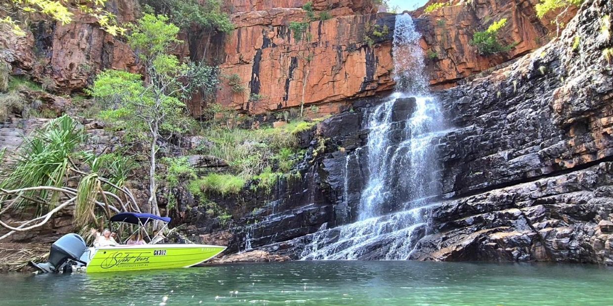 Silent Tours Boat with smiling passengers next to a spectacular Ord River waterfall