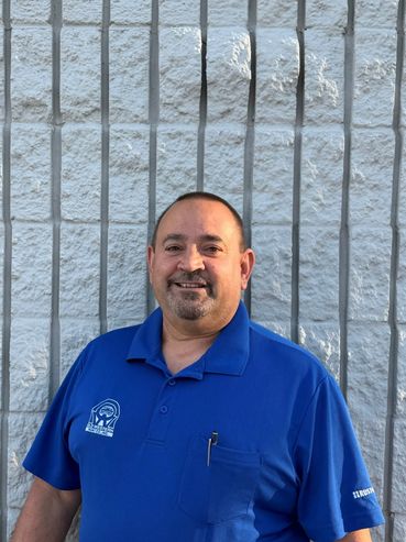 Man in blue polo shirt standing against a textured wall.