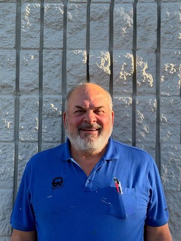 Smiling man standing against a white textured wall with metal bars.