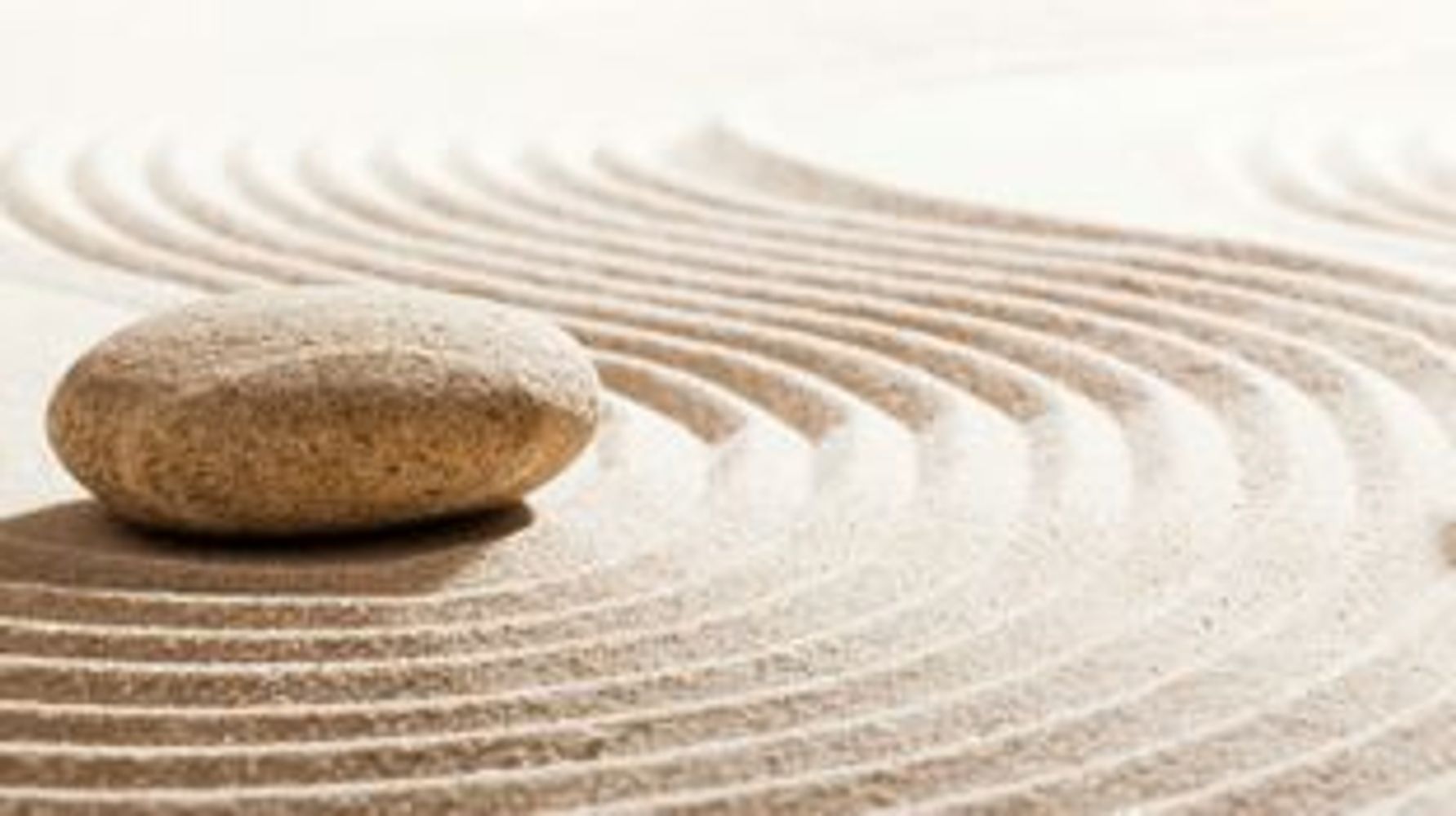 A smooth stone resting on sand with raked, curved patterns.