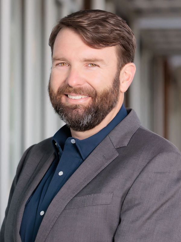 Smiling man with a beard in a grey blazer and navy shirt.