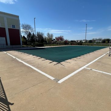 Swimming pool covered with a green safety cover on a sunny day.