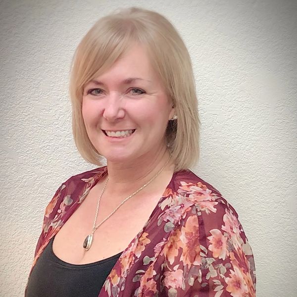Smiling woman with blonde hair in floral shawl and black top.