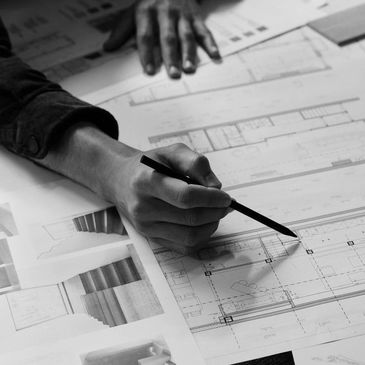 Person drawing architectural blueprints with a pencil on a desk.