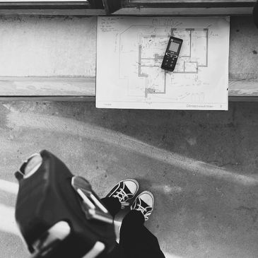 Top view of sneakers and building plan with a measuring device on a bench.