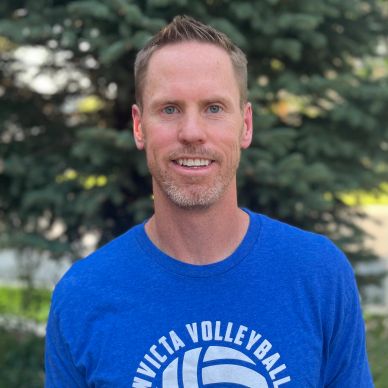 Man in a blue volleyball shirt standing outdoors with trees in the background.