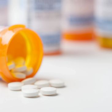 White pills spilling from an orange prescription bottle on a white surface.