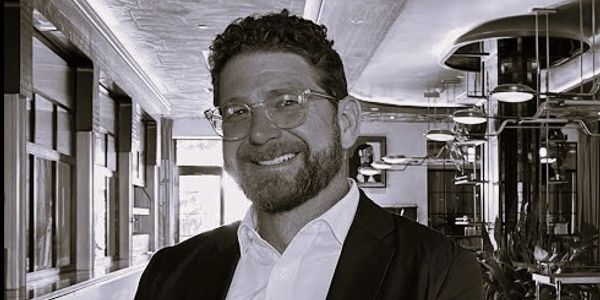 Smiling man with glasses in a suit inside a modern office space.