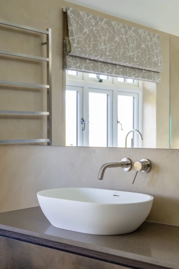 Modern bathroom sink with wall-mounted faucet and decorative window shade.