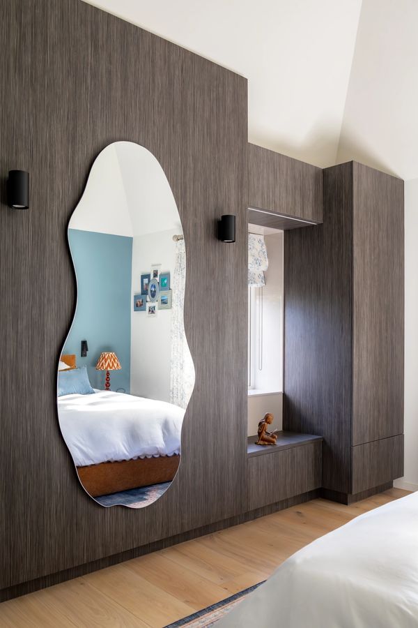 Modern bedroom with a unique wavy mirror on a textured wood wall.