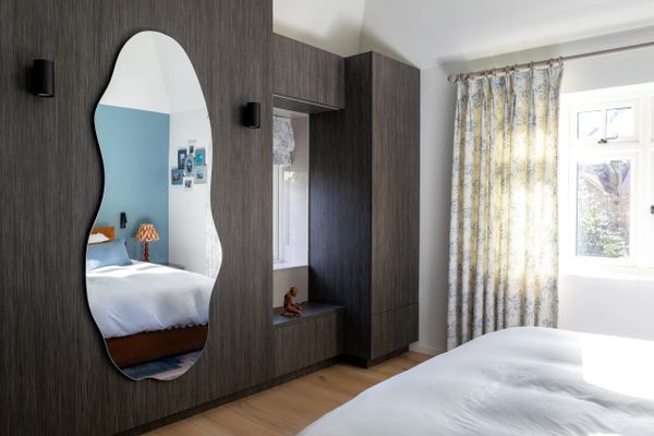 Modern bedroom with dark wood wardrobe and a uniquely shaped mirror.