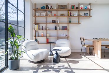 Modern living room with white chairs, wooden shelves, and large window.