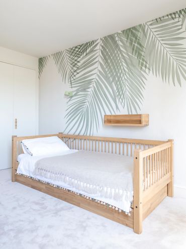 Minimalist bedroom with a wooden bed and palm leaf wall art.