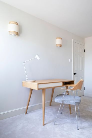 Minimalist wooden desk and chair in a bright, white room.