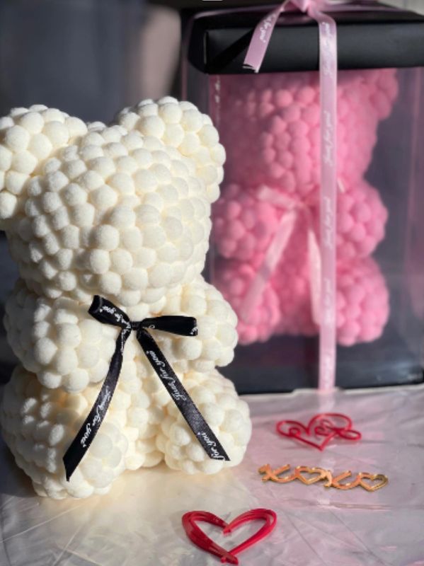 Two teddy bears made of small pom-poms, one white and one pink in a box, with decorative heart clips.