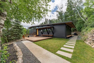 Modern black house with wooden deck and lush green yard.