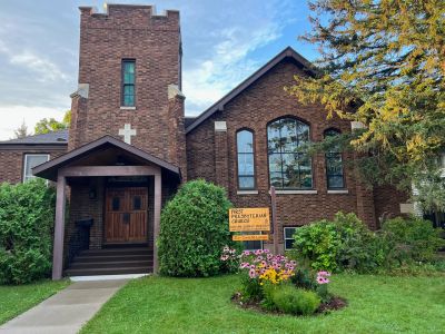 Brick First Presbyterian Church with a garden and clear sky.