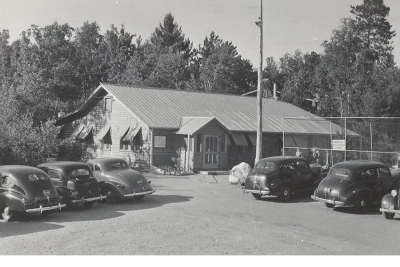 Vintage black and white photo of a rustic building with classic cars parked outside.