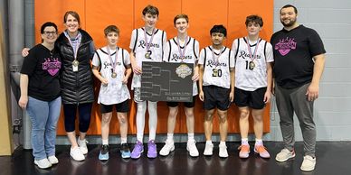 Youth basketball team posing with championship plaque and coaches indoors.