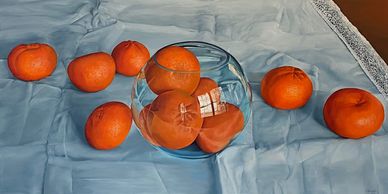 A bowl with oranges on a blue cloth surrounded by more oranges.